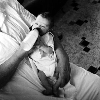 A person gently feeds a baby in bed.