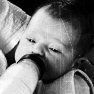 A person gently feeds a baby in bed.