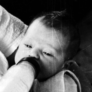 A person gently feeds a baby in bed.