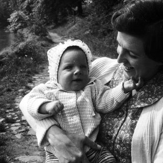 A woman joyfully holds a smiling baby outdoors.