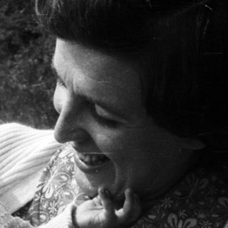 A woman joyfully holds a smiling baby outdoors.