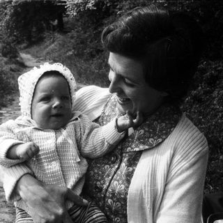 A woman joyfully holds a smiling baby outdoors.