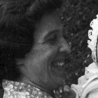 A woman holding a smiling baby outdoors.