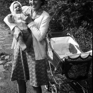 A woman holding a baby outdoors with a stroller.