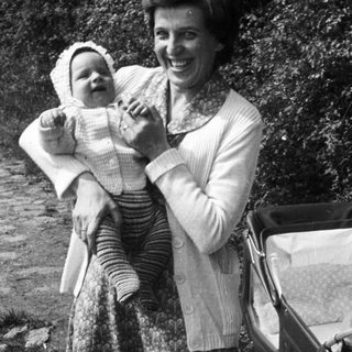 A woman holding a baby outdoors with a stroller.