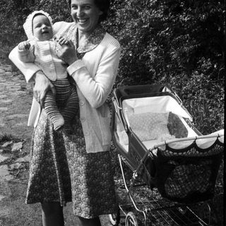 A woman holding a baby outdoors with a stroller.