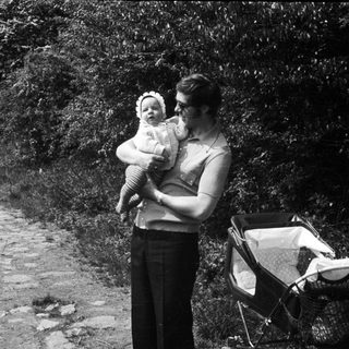 Mother holding baby outdoors near stroller.