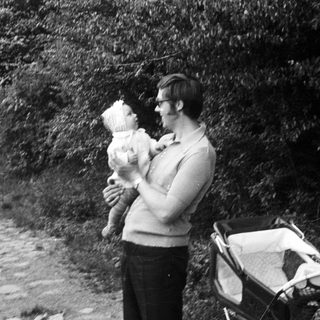 A man holding a baby outdoors near a stroller.