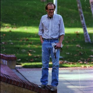 Man standing outdoors holding umbrella near wet pavement.
