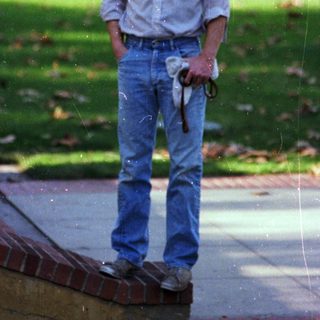 Man standing outdoors holding umbrella near wet pavement.