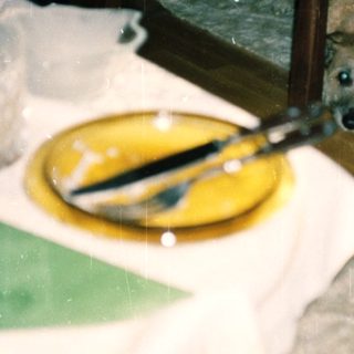 Dog peeking from under a table in a messy indoor setting.