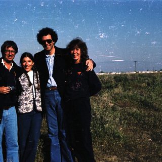 Four people posing outdoors in casual attire.