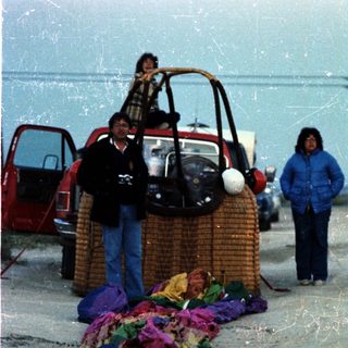 Group of people near beach with hot air balloon basket and colorful fabric.