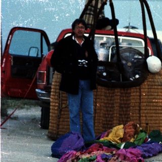 Group of people near beach with hot air balloon basket and colorful fabric.