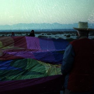 Colorful fabric drying on beach with people.