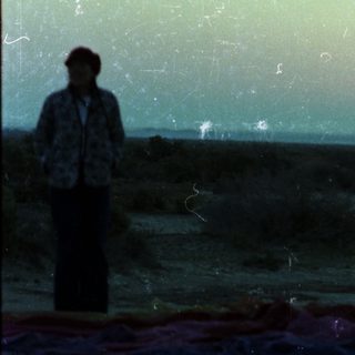 Silhouette of person standing by water at sunset.