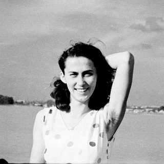 Smiling woman in vintage polka-dot dress by water.