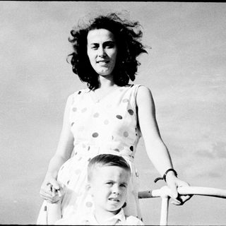Woman holding young boy on roller skates outdoors.