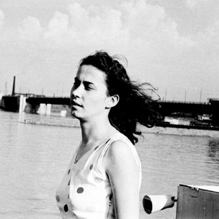Woman standing by waterfront, windblown hair.