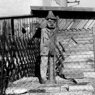 Statue of man in winter attire near fence.