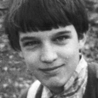 Boy in vintage sports vest, sitting outdoors.