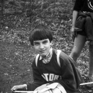 Boy in vintage sports vest, sitting outdoors.