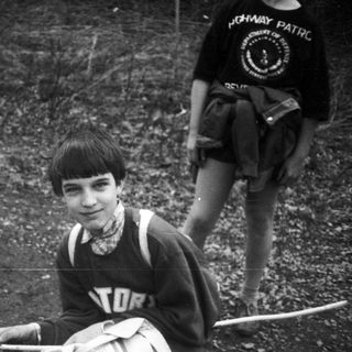 Boy in vintage sports vest, sitting outdoors.