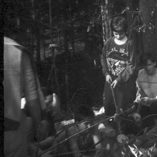 People camping by fire in forested area.