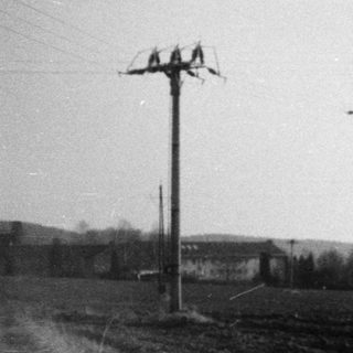 Rural landscape with power lines, fields, and distant buildings.