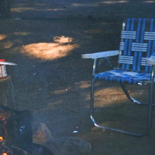 Man grilling meat over campfire outdoors.