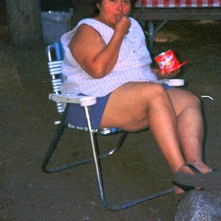Woman sitting alone outdoors at night, holding drink.