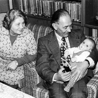 Older couple holding and smiling with baby indoors.
