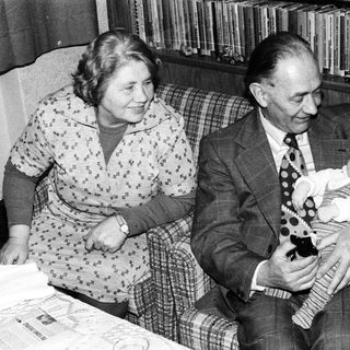 Older couple holding and smiling with baby indoors.