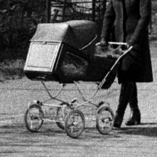 Woman pushing baby buggy with shopping cart on road.