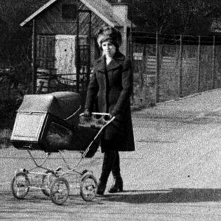 Woman pushing baby buggy with shopping cart on road.
