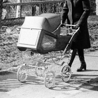 Woman pushing baby stroller outdoors in park.