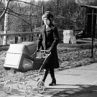 Woman pushing baby stroller outdoors in park.