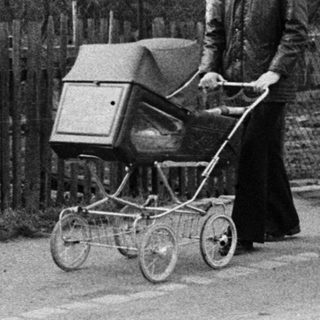 Woman pushing baby buggy on quiet road.