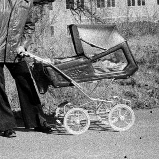 Man pushing baby buggy on rural road.
