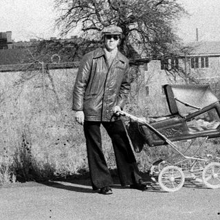 Man pushing baby buggy on rural road.