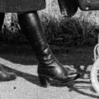 A woman in vintage clothing pushes an old-fashioned baby carriage outdoors.