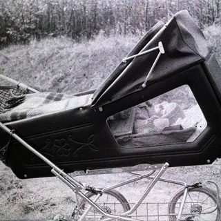 Baby carriage with open canopy showing infant inside.