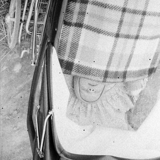 Baby sleeping in vintage pram with plaid blanket.