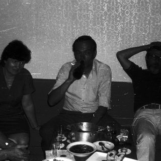 Group of five people gathered indoors, enjoying drinks and conversation.