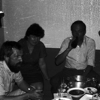 Group of five people gathered indoors, enjoying drinks and conversation.