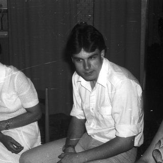 Two people sitting indoors in casual 1970s-style clothing.