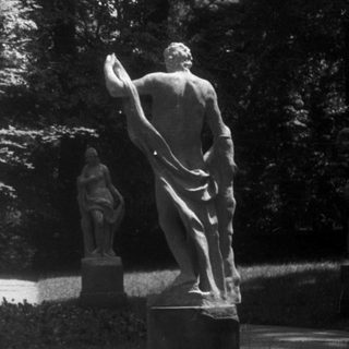 Classical statues in a shaded garden pathway.