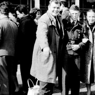 Group of people posing outside a train station in mid-20th century attire.