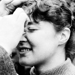 A woman being playfully kissed on the forehead by someone outdoors.