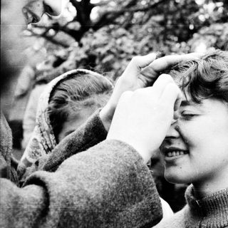 A woman being playfully kissed on the forehead by someone outdoors.